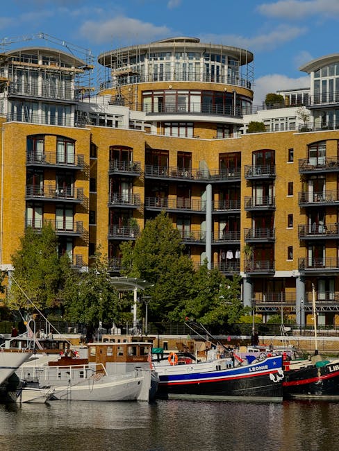 A view of modern residential buildings with yellow brick facades and large glass windows, situated along a waterfront with several docked boats, including one named Leonie. The buildings feature multi